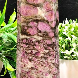 Puede incluir: Un obelisco de piedra pulida y alta con una parte superior facetada. La piedra presenta una mezcla de colores rosa, marrón y crema, con un patrón moteado. El obelisco es un objeto decorativo.