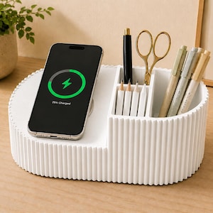 May include: A white oval desk organizer with a ribbed exterior featuring a built-in wireless charging pad for a smartphone and multiple compartments for stationery items including pens, pencils, and gold-toned scissors.