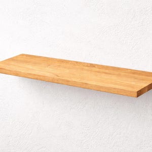 Peut inclure: Une étagère rectangulaire en bois, présentant un fini veiné naturel. L'étagère est fixée sur un mur blanc texturé, offrant une esthétique épurée et minimaliste. L'étagère mesure environ 76 cm de long.