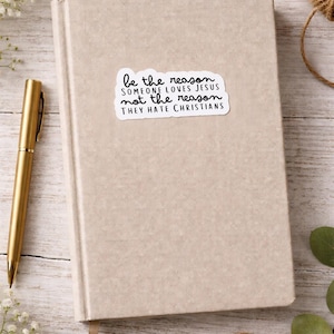Könnte beinhalten: Ein beiges Hardcover-Notizbuch mit einem Aufkleber mit der Aufschrift "be the reason someone loves Jesus not the reason they hate Christians". Ein goldener Stift liegt neben dem Notizbuch. Das Notizbuch hat ein beiges Leseband.
