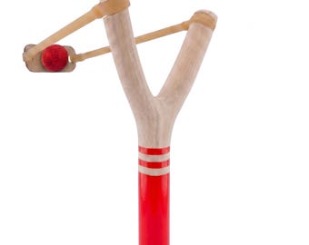 May include: A wooden slingshot with a red and white striped handle and a red ball. The slingshot has a Y-shaped frame with tan rubber bands and a small leather pouch to hold the projectile.
