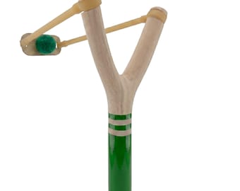 May include: A wooden slingshot with a green handle and two white stripes. The slingshot has a light brown rubber band and a green projectile. The slingshot is a classic toy.