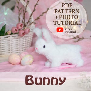 Puede incluir: Un conejito de peluche blanco con detalles rosas y dos huevos de Pascua decorados sobre una superficie rosa. Una cesta blanca con flores rosas y vegetación en el fondo. El texto dice "PDF Pattern + Photo Tutorial" y "Bunny".