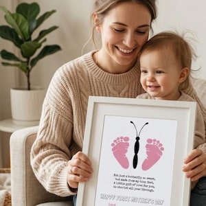 Könnte beinhalten: Ein weiß gerahmter Druck mit einem Schmetterlingsdesign aus rosa Fußabdrücken und einem schwarzen Körper. Der Text lautet "Happy First Mother's Day" und ein Gedicht.