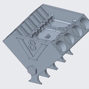 Könnte beinhalten: Ein hellgraues, 3D-gedrucktes V8-Motorblockmodell mit vier kreisförmigen Zylinderöffnungen auf jeder Seite, einem markanten V8-Emblem auf der Vorderseite und den Buchstaben MP auf der Innenfläche des Motorraums.