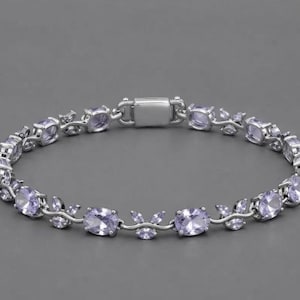 May include: A silver-toned bracelet featuring a series of oval-shaped, light purple gemstones alternating with small, leaf-like silver accents. The bracelet is secured with a rectangular box clasp and has a continuous, symmetrical link design.