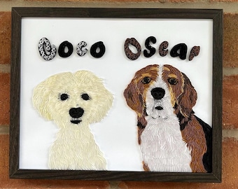 May include: A framed paper art piece featuring two dogs, Coco and Oscar. The dogs are made of paper and have a realistic appearance. The names Coco and Oscar are written in black paper letters above the dogs.