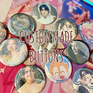 May include: A collection of circular pin-back buttons featuring various printed illustrations of people and characters, with a holographic finish. The text CUSTOM MADE BUTTONS is overlaid in the center of the image in a brown font.