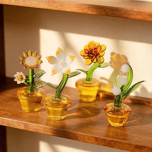 May include: A white ceramic mug with a black handle and the text "But First, Coffee" in a bold, black font. The mug is set against a blurred background, suggesting a cosy setting.