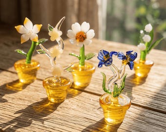 May include: A collection of five glass flower sculptures in small yellow pots. The flowers are various colors, including white, yellow, and blue, with green stems and leaves. The glass is transparent, and the pots are a solid yellow.
