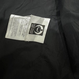 May include: Close-up of a black fabric with two white tags. One tag has text in multiple languages and the other tag has the words "FAIR TRADE CERTIFIED" and a logo.