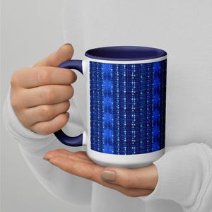 May include: A white ceramic mug with a black handle and the text "But First, Coffee" in a bold, black font. The mug is set against a blurred background, suggesting a cosy setting.