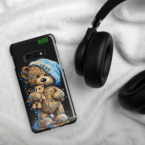May include: A black smartphone case featuring a graphic of a brown teddy bear wearing a blue knit hat and holding a smaller teddy bear. The design includes blue and yellow paint splatters and the green text "ESE" at the top and on the hat.
