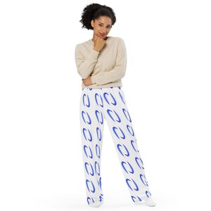 May include: White pajama pants with a repeating pattern of blue oval shapes. The pants are wide-legged and worn with a beige long-sleeved shirt. The model is standing and smiling.