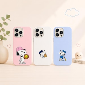 Puede incluir: Tres fundas para teléfono en rosa, blanco y azul, cada una con un diseño de béisbol de Snoopy. La funda rosa muestra a Snoopy con un guante y una gorra de béisbol. La funda blanca tiene a Snoopy con un guante. La funda azul tiene a Snoopy con un bate.