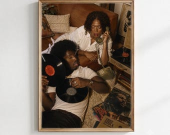 Puede incluir: Una impresión artística enmarcada que muestra a dos personas en una habitación de tonos cálidos. Una persona lleva una camisa blanca y sostiene un teléfono de disco vintage, mientras que la otra lleva una camisa blanca y sostiene un disco de vinilo.