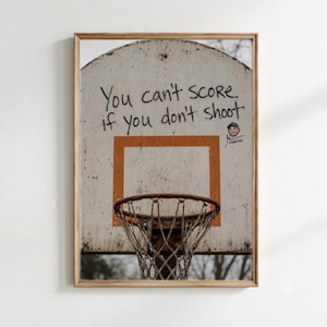 Könnte beinhalten: Ein gerahmter Wandkunstdruck, der ein verwittertes, cremefarbenes Basketball-Backboard mit einem abgenutzten orangefarbenen Quadrat und einem Metallkorb zeigt. Der Text "You can't score if you don't shoot" ist in schwarzem Marker geschrieben.
