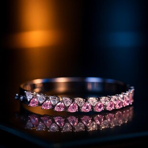 May include: A silver bracelet featuring alternating pink and clear teardrop-shaped gemstones. The bracelet is presented on a reflective surface, against a dark backdrop with orange and blue gradient lighting.