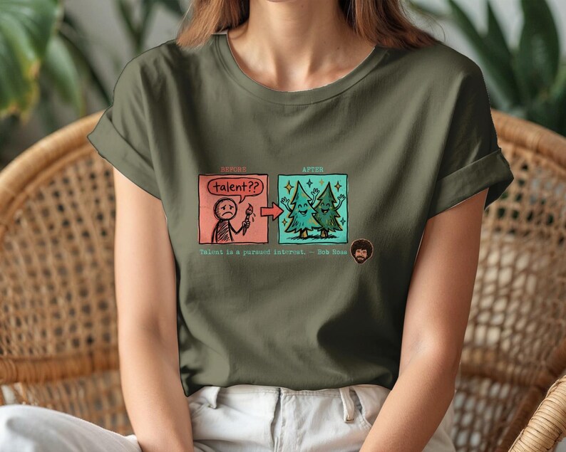 A streetwear-style t-shirt featuring a Y2K cyber-graphic with a portrait of Bob Ross and the quote "Talent is a pursued interest" in bold typography.