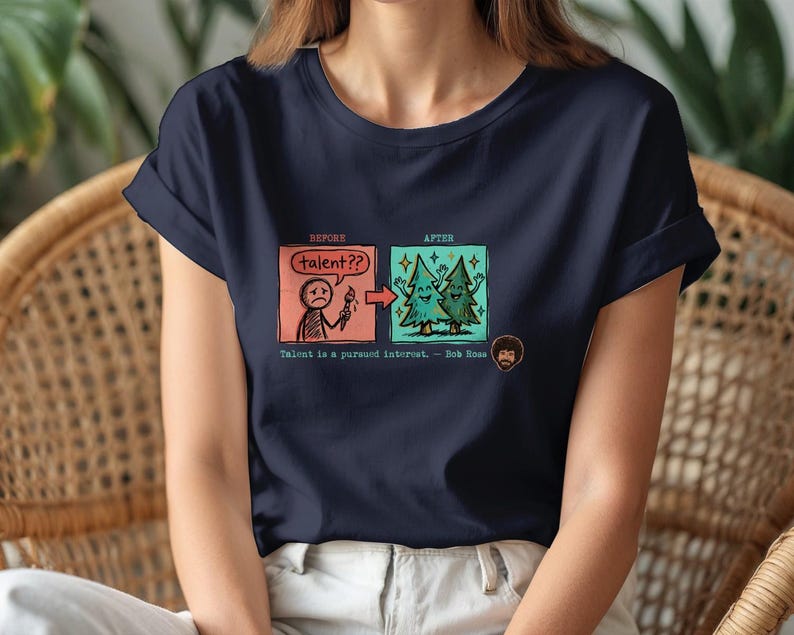 A streetwear-style t-shirt featuring a Y2K cyber-graphic with a portrait of Bob Ross and the quote "Talent is a pursued interest" in bold typography.
