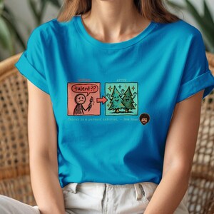 A streetwear-style t-shirt featuring a Y2K cyber-graphic with a portrait of Bob Ross and the quote "Talent is a pursued interest" in bold typography.