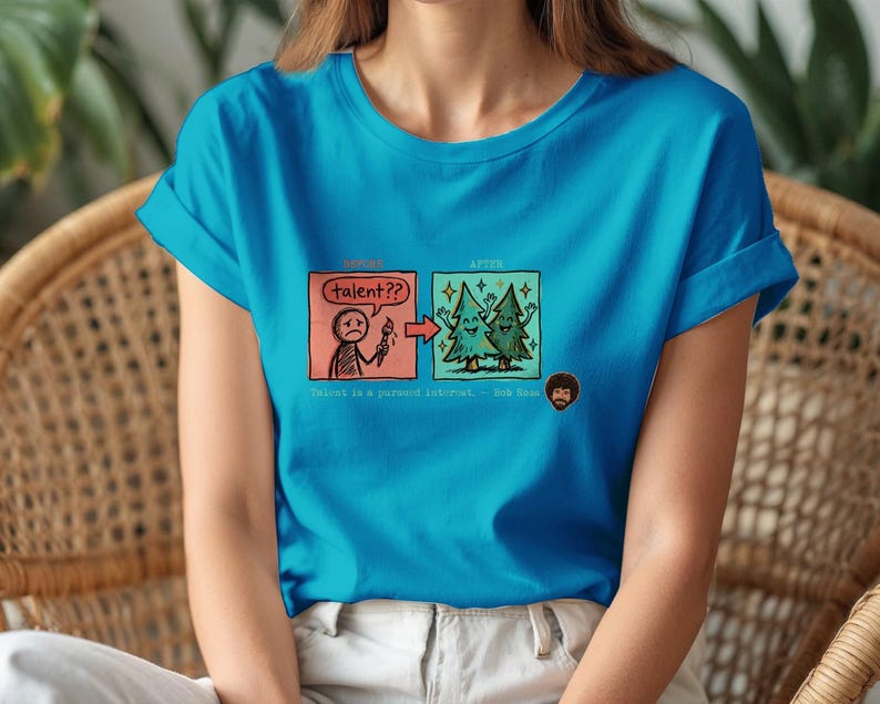A streetwear-style t-shirt featuring a Y2K cyber-graphic with a portrait of Bob Ross and the quote "Talent is a pursued interest" in bold typography.