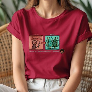 A streetwear-style t-shirt featuring a Y2K cyber-graphic with a portrait of Bob Ross and the quote "Talent is a pursued interest" in bold typography.