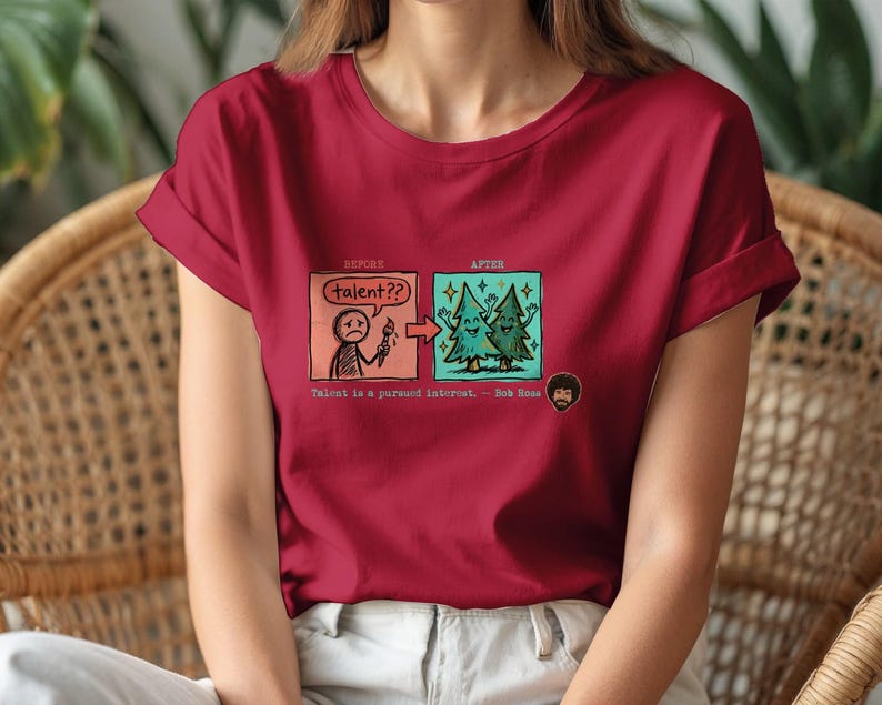 A streetwear-style t-shirt featuring a Y2K cyber-graphic with a portrait of Bob Ross and the quote "Talent is a pursued interest" in bold typography.