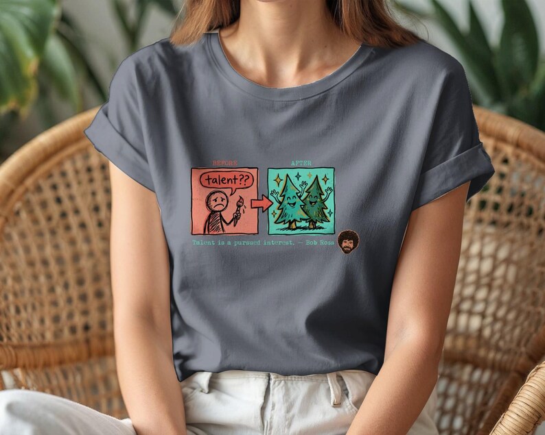A streetwear-style t-shirt featuring a Y2K cyber-graphic with a portrait of Bob Ross and the quote "Talent is a pursued interest" in bold typography.