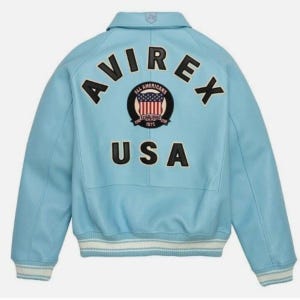 Może przedstawiać: Jasnoniebieska sk&oacute;rzana kurtka z napisem "AVIREX USA" na plecach. Kurtka posiada kołnierz, prążkowane mankiety oraz naszywkę z amerykańską flagą. Kurtka ma klasyczny styl bomber.