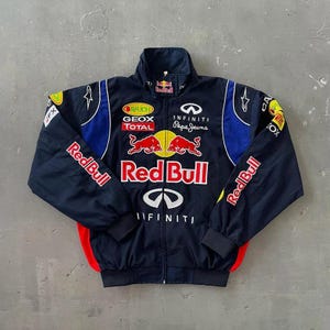 Puede incluir: Chaqueta de carreras Red Bull azul marino con detalles rojos, amarillos y blancos. Presenta el logotipo de Red Bull, la marca Infiniti y Pepe Jeans. Incluye cuello alzado y cremallera completa.