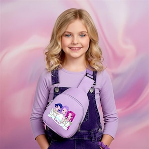 May include: A light purple sling bag with a cartoon graphic of three girls, worn across the body. The bag has a zipper closure and a strap. The girl in the image is wearing a purple long-sleeve shirt and denim overalls.