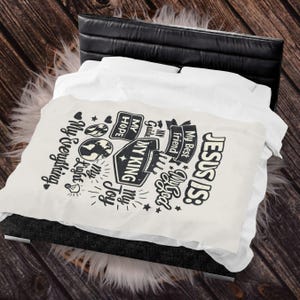 May include: A white blanket with black text that reads "JESUS IS: My Best Friend, My God, My King, My Guide, My Hope, My Joy, My Light, My Everything." The blanket is on a bed with a black headboard.