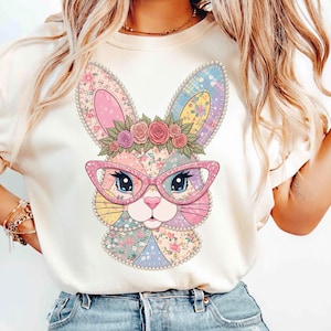 Op de afbeelding: Crèmekleurig T-shirt met een kleurrijk patchwork konijnengezicht. Het konijn draagt een roze bril en een bloemenkrans. Het ontwerp heeft bloempatronen in pastelkleuren en is gecentreerd op het T-shirt. Het konijn heeft blauwe ogen.