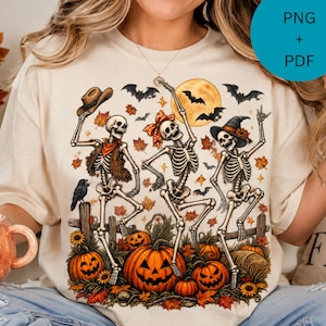 Pode incluir: Uma t-shirt cor de creme com um gráfico de três esqueletos a dançar num cenário de outono. Os esqueletos usam um chapéu de cowboy, um laço no cabelo e um chapéu de bruxa. A cena inclui abóboras, folhas de outono, morcegos e lua cheia.