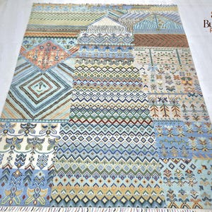 May include: A large, rectangular area rug with a patchwork design. The rug features a variety of geometric and floral patterns in shades of blue, beige, orange, and green. The rug has a fringed edge and is suitable for a living room or bedroom.