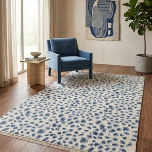 Op de afbeelding: Een rechthoekig vloerkleed met een herhalend blauw luipaardpatroon op een crèmekleurige achtergrond. Het kleed is afgewerkt met korte, lichtgekleurde franjes langs de twee kortere zijden, wat zorgt voor een textuurrijke rand aan het ontwerp.