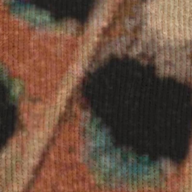 Op de afbeelding: Close-up van een textiel met een tie-dye patroon. De kleuren zijn bruin, zwart en blauwgroen. De stof lijkt gebreid of geweven te zijn, met zichtbare verticale lijnen.