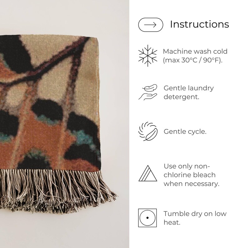 Op de afbeelding: Een rechthoekige sprei met een vlindervleugelontwerp in bruin, zwart en blauwgroen. De sprei heeft een gefranjerde rand en het woord "Instructions" is zichtbaar. Wasvoorschriften zijn ook inbegrepen.