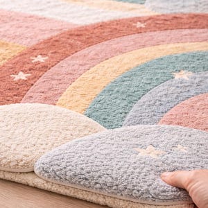 May include: A colorful, soft rug with a rainbow design. The rug features pastel colors including pink, yellow, green, and blue. The rug also has cloud-shaped accents and star details.