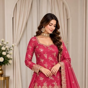 May include: A vibrant fuchsia sharara suit featuring a long-sleeved tunic and wide-leg trousers adorned with intricate gold embroidery and reflective mirror work. The ensemble includes a matching sheer dupatta with a heavy gold embroidered border.