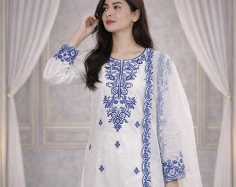 Könnte beinhalten: Weißer bestickter Anzug mit blauen Blumenmustern. Das Outfit umfasst ein langärmliges Oberteil, eine Hose mit weitem Bein und einen transparenten Schal. Die Stickerei ist detailliert und bedeckt den Ausschnitt, die Ärmel und den Hosenbund.