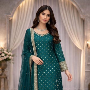 Può includere: Un completo salwar kameez verde acqua con abbellimenti dorati. L'outfit comprende una tunica a maniche lunghe, pantaloni abbinati e un dupatta trasparente. La tunica e il dupatta sono adornati da intricati dettagli dorati. L'outfit è indossato da una persona.
