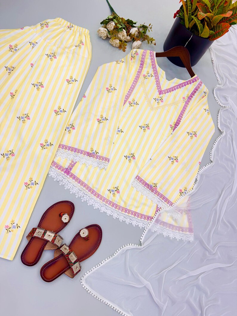 K&ouml;nnte beinhalten: Ein gelb-wei&szlig; gestreiftes Tunika- und Hosenset mit kleiner Blumenstickerei, lila Besatz und wei&szlig;er Spitzenverzierung an Saum und &Auml;rmeln, dazu ein Paar braune Sandalen und ein wei&szlig;er, transparenter Dupatta.