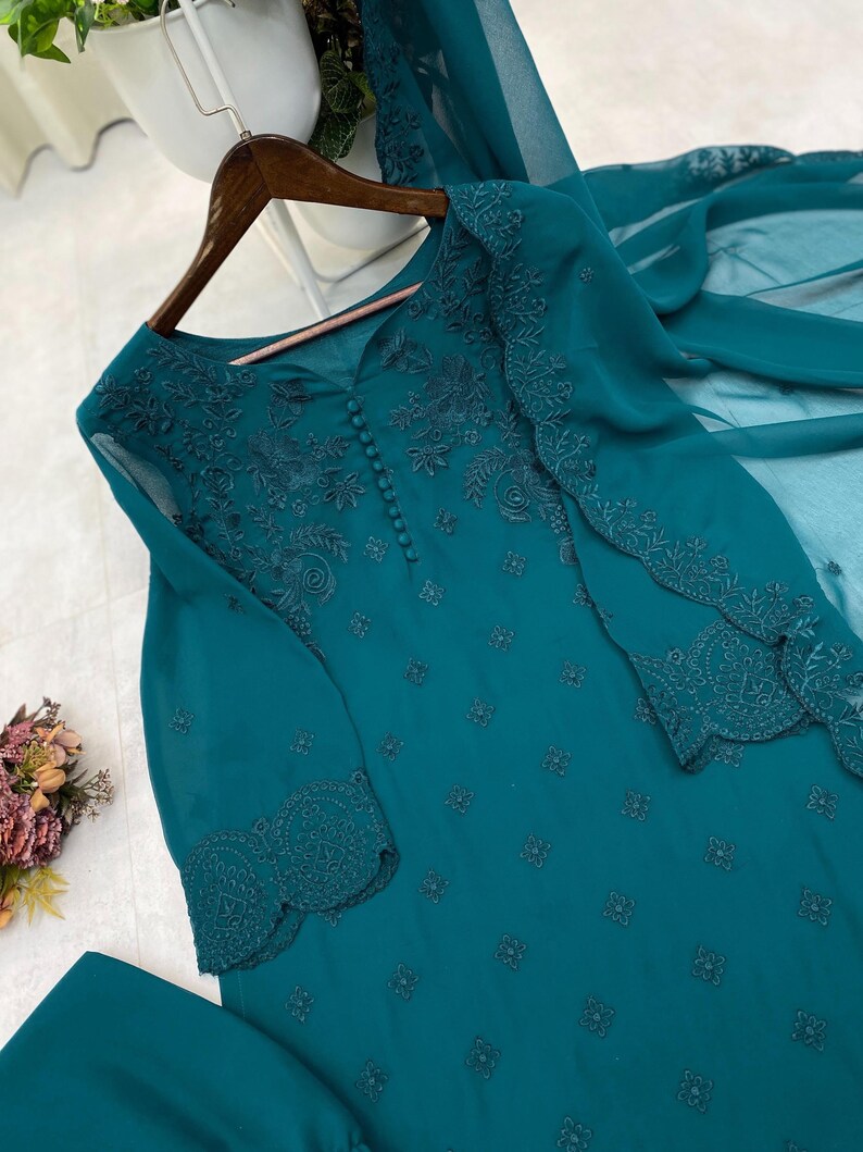 May include: A teal long-sleeved tunic featuring intricate tonal embroidery, a row of small fabric-covered buttons down the center chest, and scalloped cuffs. The garment is made of a sheer, lightweight fabric and includes a matching sheer scarf.