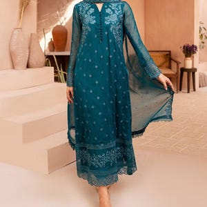 May include: A long-sleeved teal dress featuring intricate tonal floral embroidery on the bodice and hem, a notched neckline with a vertical row of small buttons, and a sheer, flowing overlay that extends into a draped panel on the side.