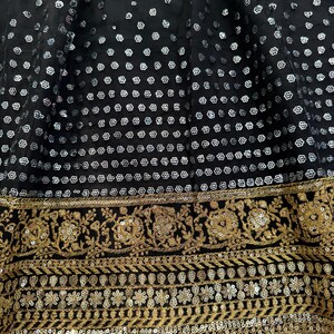 Peut inclure: Gros plan sur un tissu noir orn&eacute; de sequins argent&eacute;s dispos&eacute;s en motif. Le bord inf&eacute;rieur pr&eacute;sente une bordure brod&eacute;e dor&eacute;e avec des motifs floraux et g&eacute;om&eacute;triques. Id&eacute;al pour v&ecirc;tements ou d&eacute;corations.