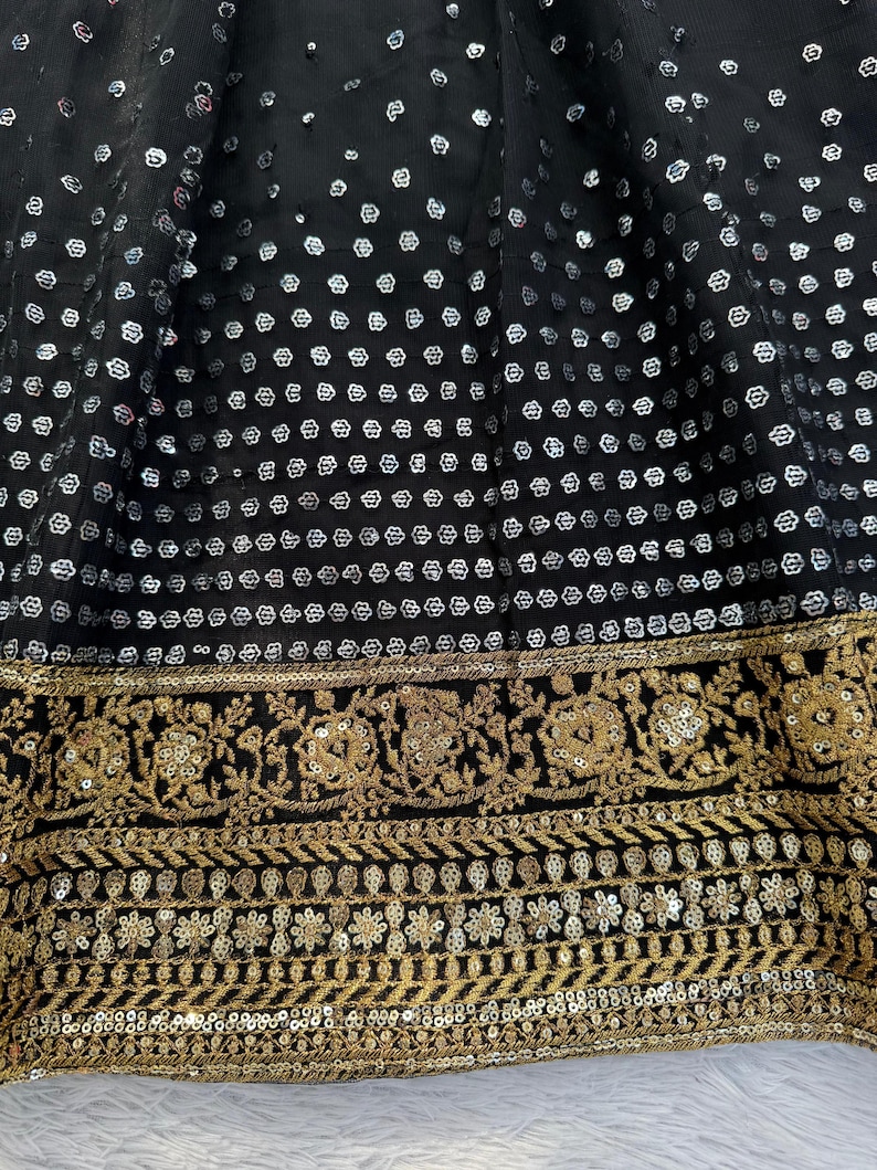 Peut inclure: Gros plan sur un tissu noir orn&eacute; de sequins argent&eacute;s dispos&eacute;s en motif. Le bord inf&eacute;rieur pr&eacute;sente une bordure brod&eacute;e dor&eacute;e avec des motifs floraux et g&eacute;om&eacute;triques. Id&eacute;al pour v&ecirc;tements ou d&eacute;corations.