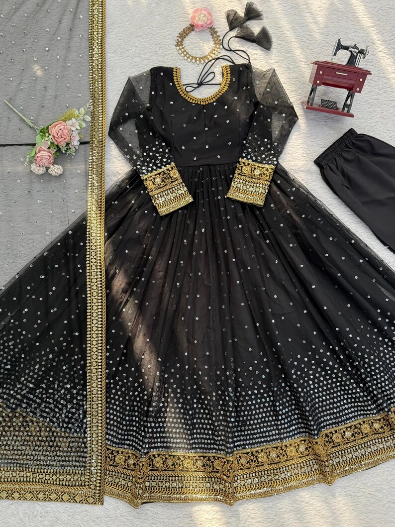 Peut inclure: Robe de soir&eacute;e noire &agrave; manches longues, orn&eacute;e de paillettes argent&eacute;es et de broderies dor&eacute;es. La robe pr&eacute;sente une jupe ample et est associ&eacute;e &agrave; un pantalon noir assorti et &agrave; une &eacute;charpe transparente &agrave; bordure dor&eacute;e. Un collier dor&eacute; et un accessoire floral pour les cheveux compl&egrave;tent l'ensemble.