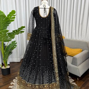 Peut inclure: Longue robe noire avec des manches longues et transparentes et un col rond. La robe est orn&eacute;e de paillettes argent&eacute;es et de broderies dor&eacute;es le long de l'ourlet et des poignets. Une &eacute;charpe transparente noire assortie avec une bordure dor&eacute;e.
